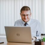 Business professional working on laptop at office desk with coffee and plants.